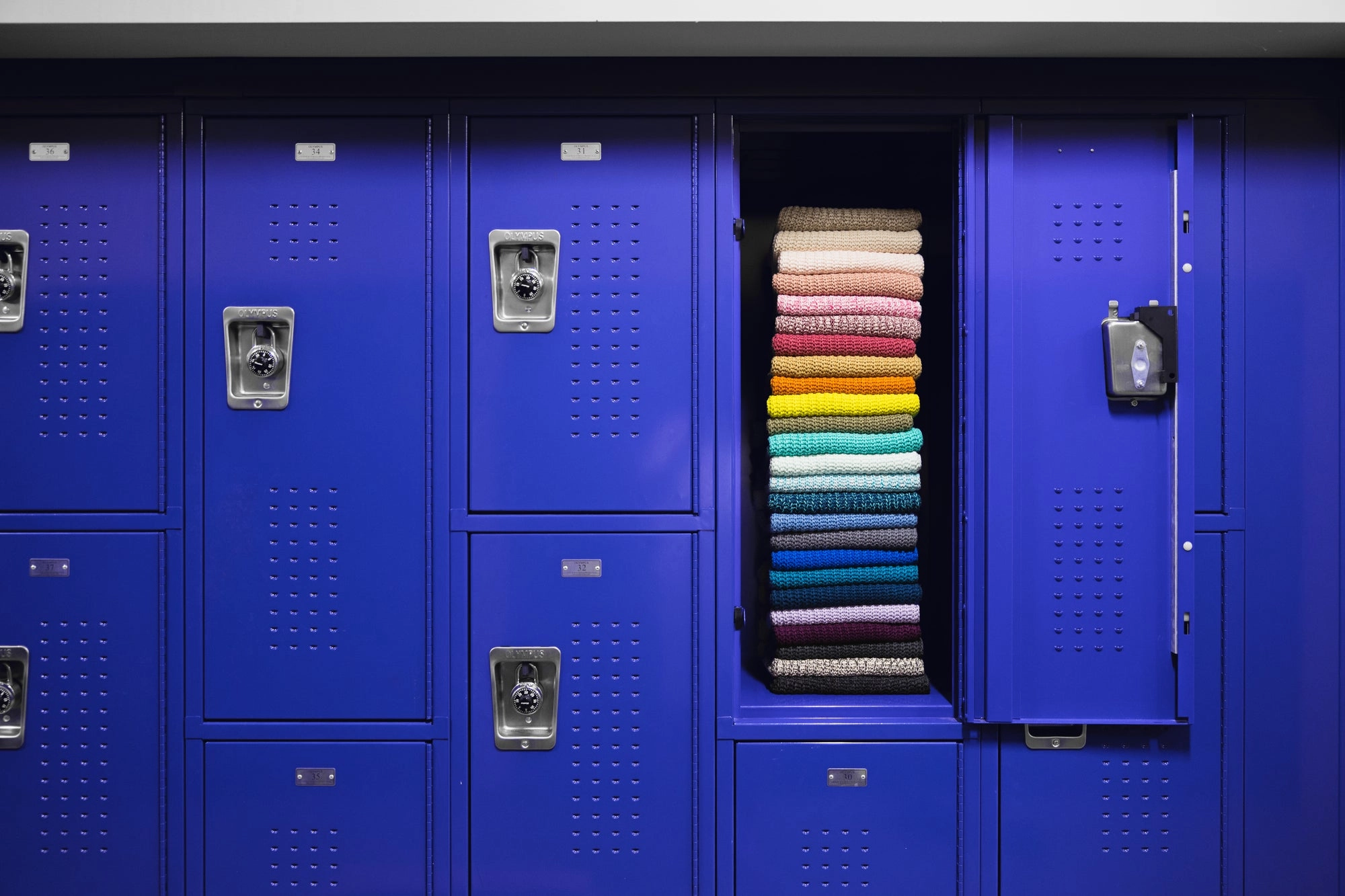 Indigo lockers, one open with a stack of folded knit beanies in every color