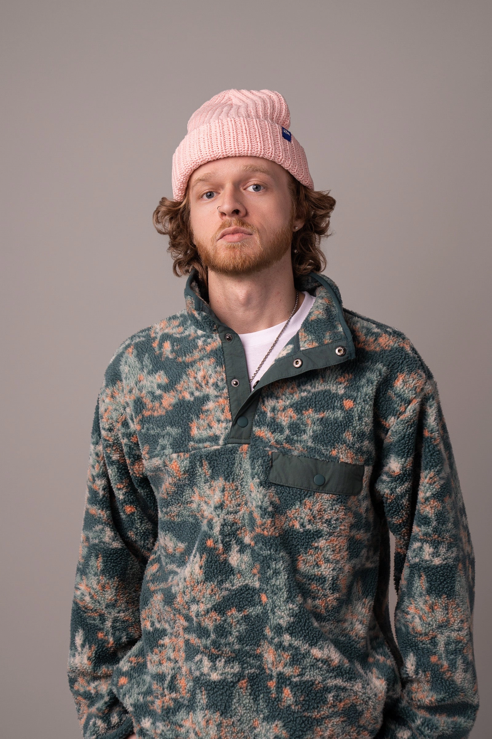 A man smiling in a blush LYM beanie and a camo fleece