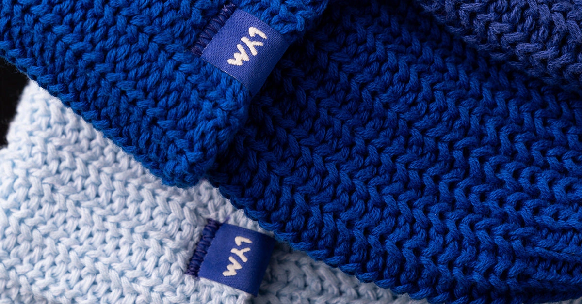 Close view of blue and white knit beanies with the blue LYM fold over label
